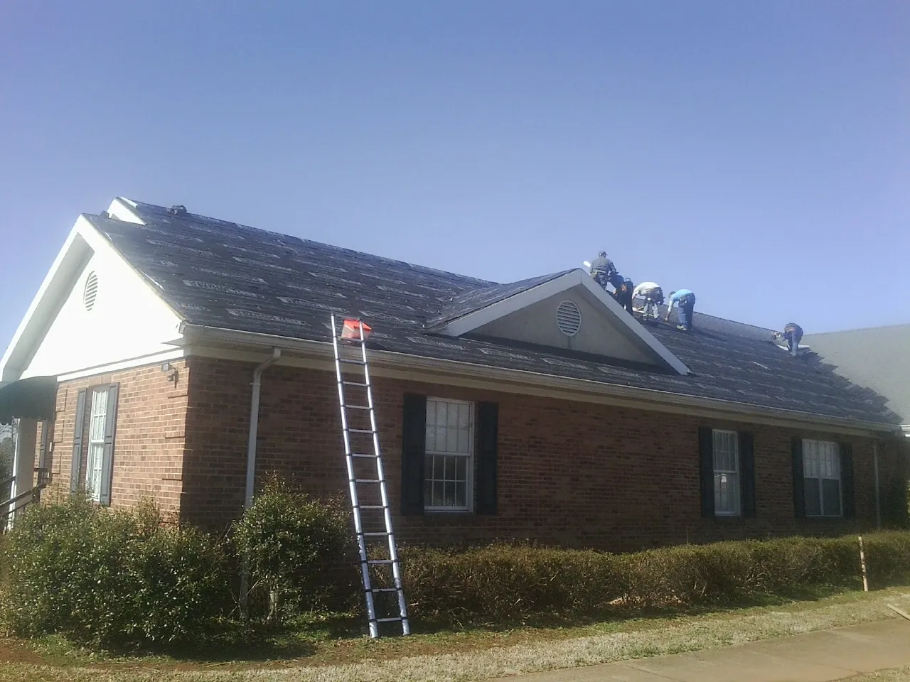 Crew tearing shingles off a brick ranch roof with a ladder set — Emergency Roof Repair work by our crew in Saint Charles